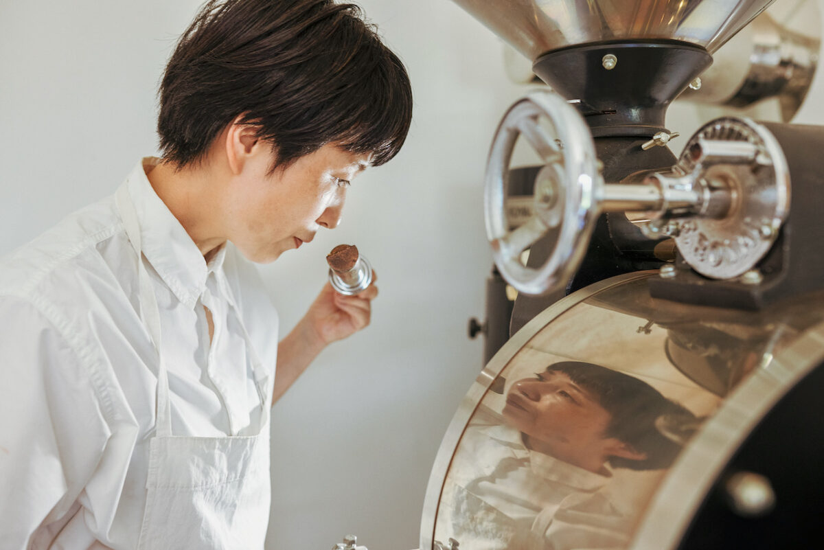 A person in a white shirt examining roasted coffee beans next to a professional coffee roaster