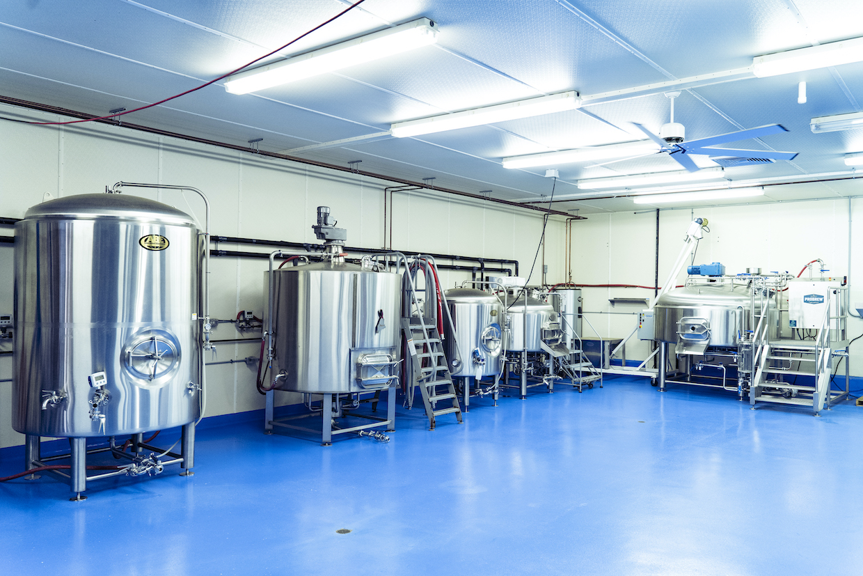 A professional cold-brew coffee production facility with stainless steel tanks, brewing equipment, and blue epoxy flooring; the source page explicitly