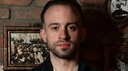 Ben Yabrow, a professional portrait against an exposed brick wall with vintage framed photographs.