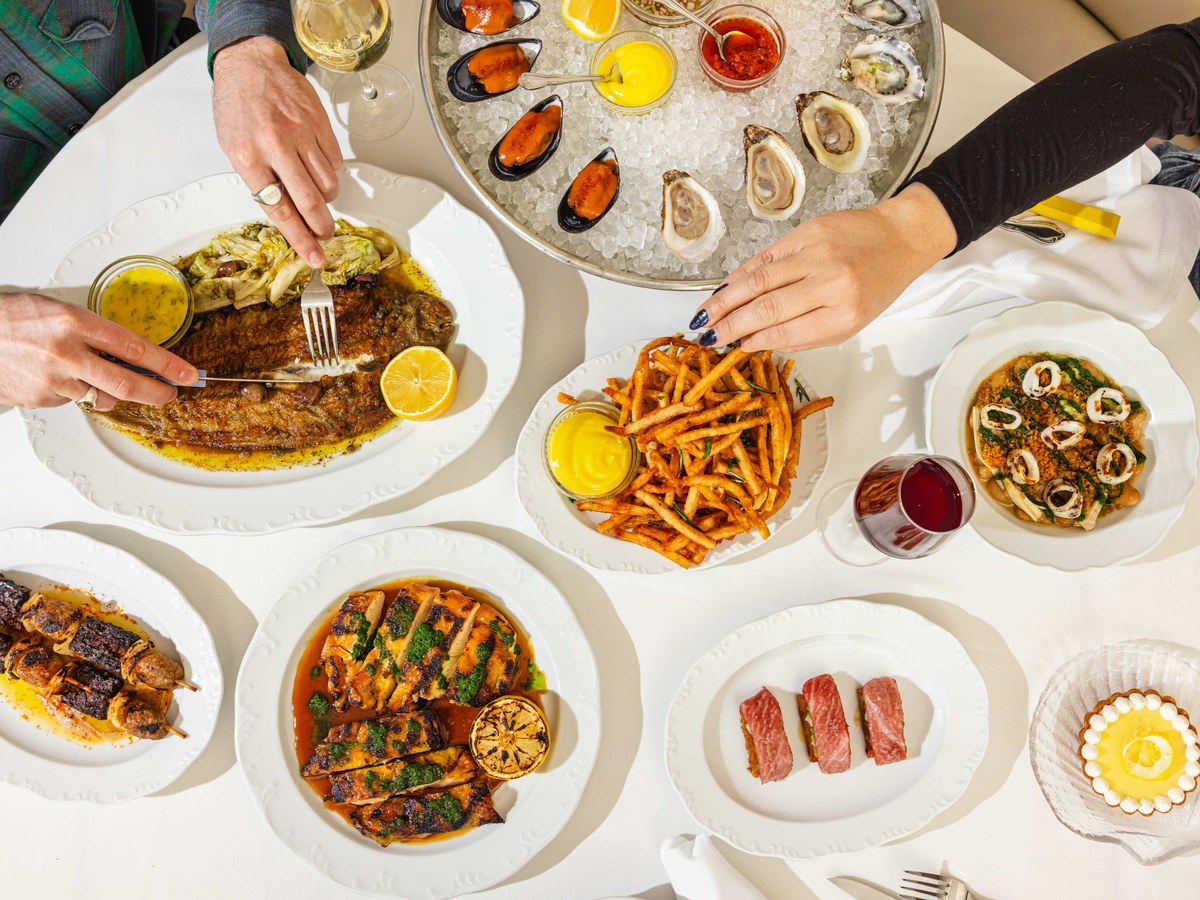 A spread of dishes from Crevette with hands taking the Dover sole and a frite at Sip & Guzzle.