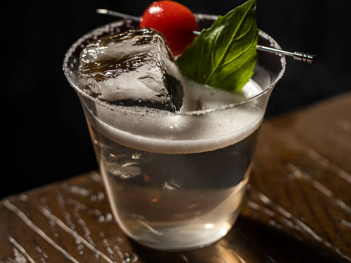 Sip & Guzzle serves a cocktail with a large ice cube, garnished with a cherry tomato and basil leaf.