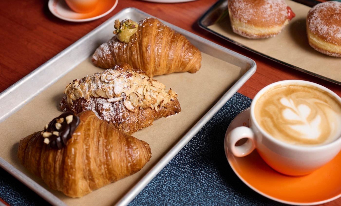 An assortment of pastries including croissants and almond-topped pastries on a tray alongside coffee drinks, published on NRN with page title explicit