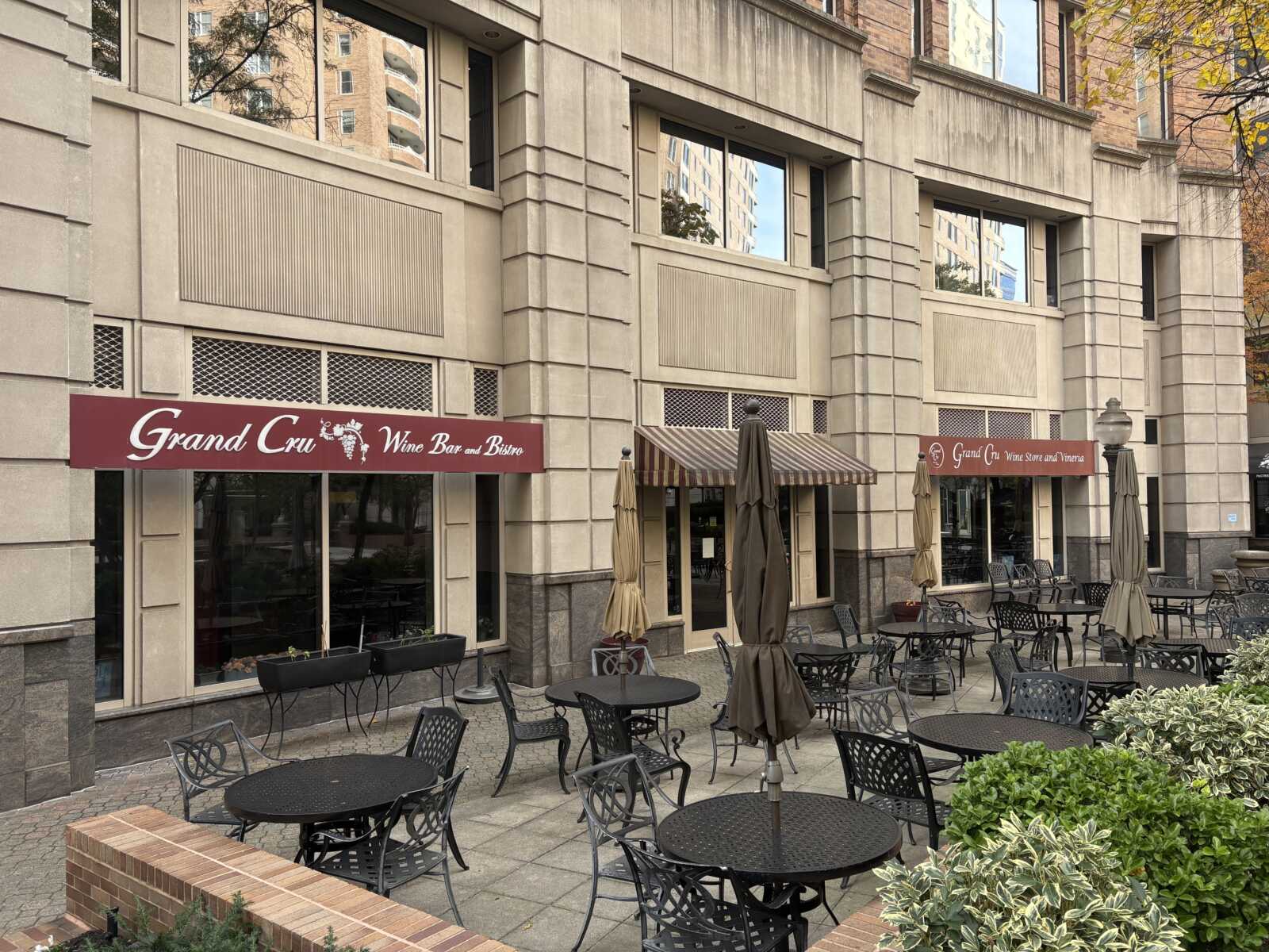 Grand Cru Wine Bar and Bistro storefront with burgundy awning, outdoor patio seating, and striped umbrellas on brick courtyard.