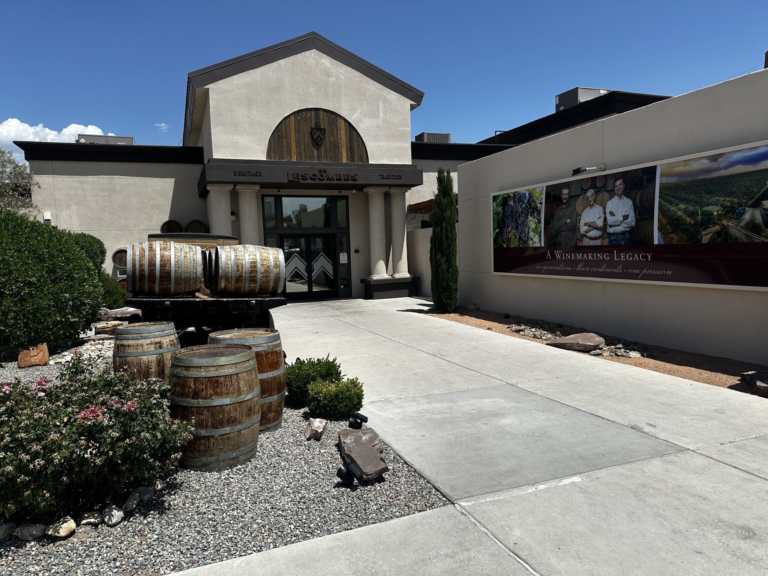 Winery entrance with wooden wine barrels and 'A Winemaking Legacy' signage under clear blue sky