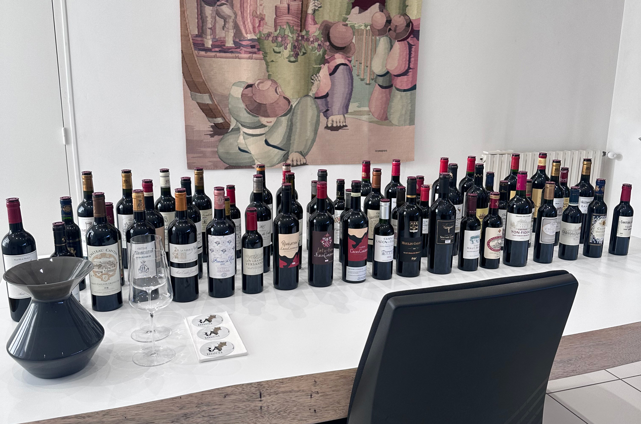 Bordeaux wine bottles lined up on white table for tasting, with empty glasses and tasting notes visible