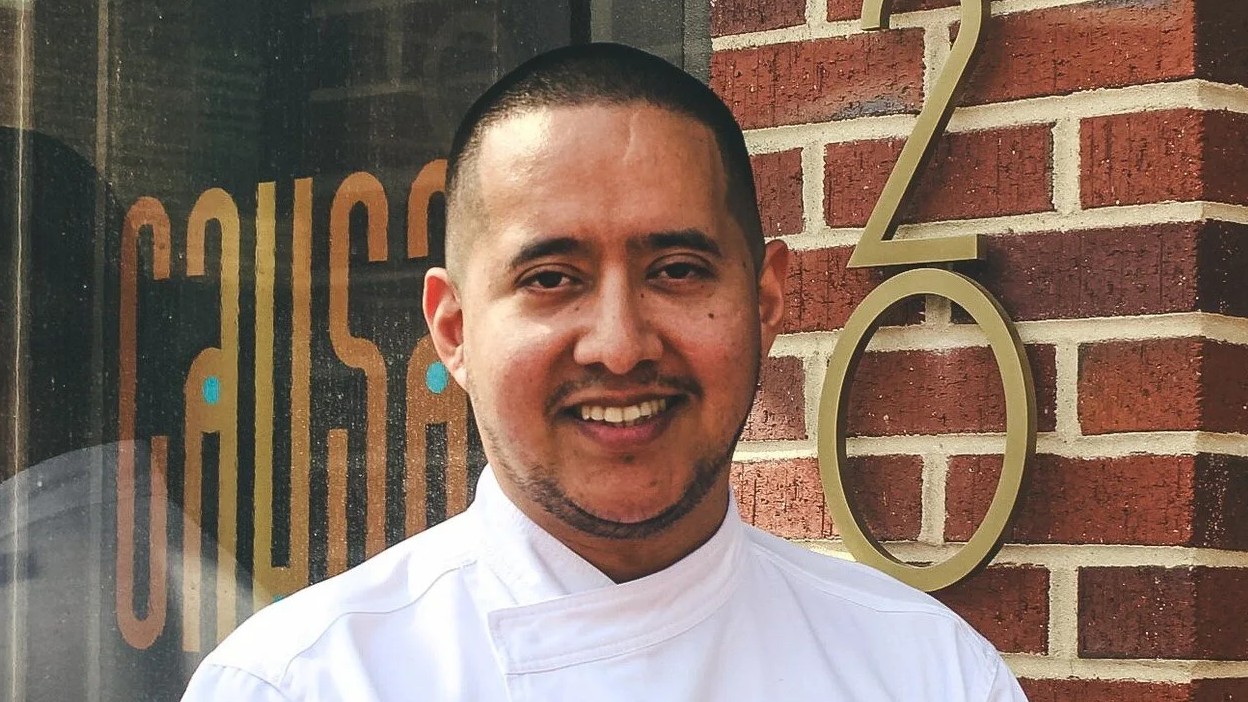 Carlos Delgado, culinary director of Brisa, smiles outside a restaurant with "CAUSA" signage.