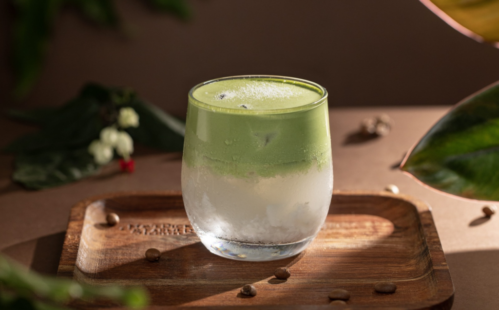 A layered matcha beverage in a clear glass on a wooden board