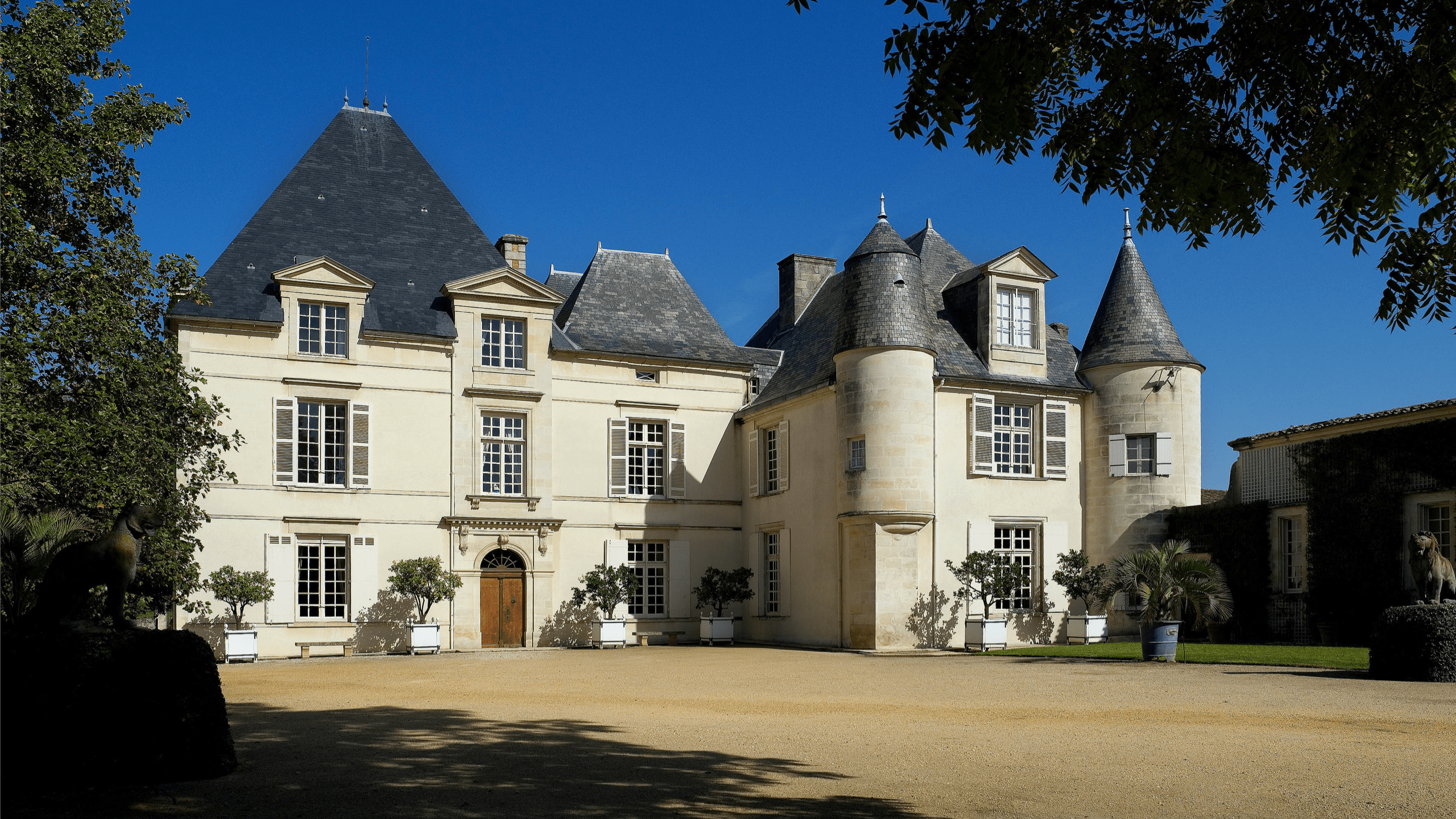 Château Haut-Brion features distinctive slate-grey turrets under a brilliant blue sky.
