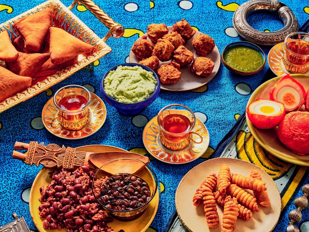 A vibrant overhead spread of Somali and East African dishes including samosas, fried fritters, bean dishes, pickled eggs, green chutneys, tea glasses,