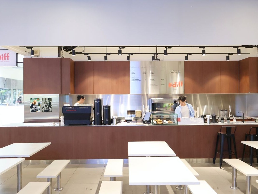 Modern coffee shop interior with copper-toned counter, white tables, and '#diff' signage visible on the back wall; source page explicitly names Diff s