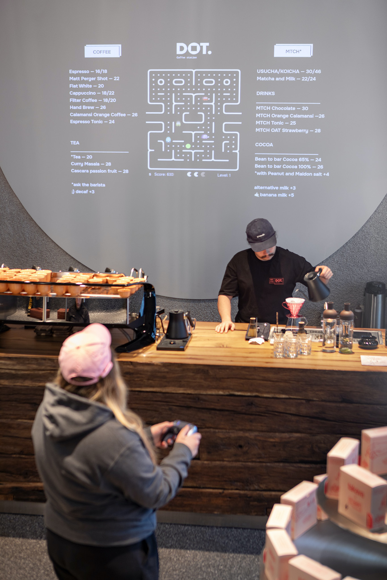 Interior shot of a coffee bar counter with reclaimed wooden beams, showing a barista preparing coffee with a pink V60 dripper, coffee equipment on the