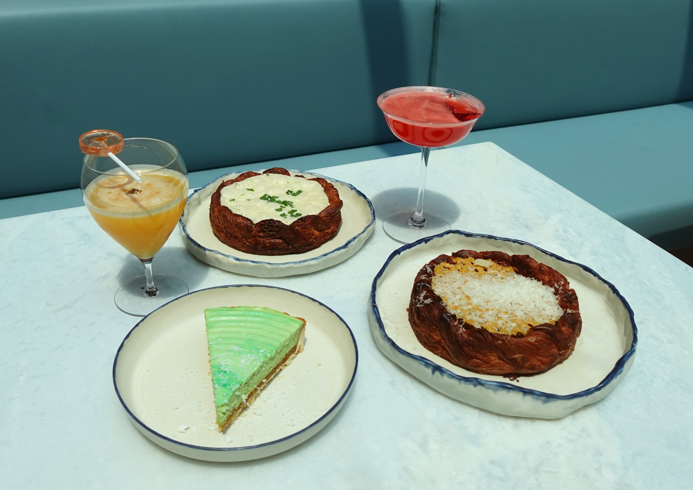 Three dessert plates and two craft cocktails/mocktails on a marble table in a modern cafe setting; the source page explicitly attests this is from Eli