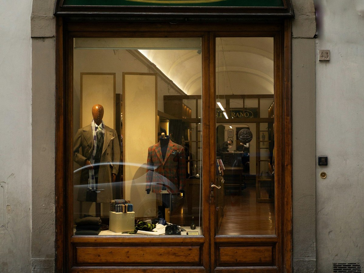 The arched entrance of Liverano & Liverano on Via dei Fossi, with its green oval sign and two mannequins in suits visible through the glass.