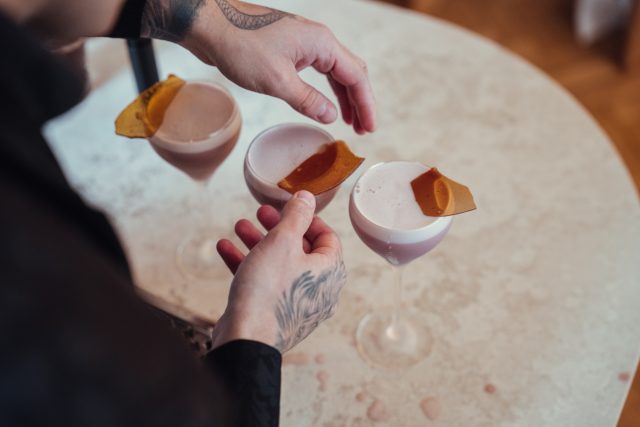 A bartender garnishes three elegant cocktails with orange peels, showcasing a blend of craftsmanship and vibrant presentation.