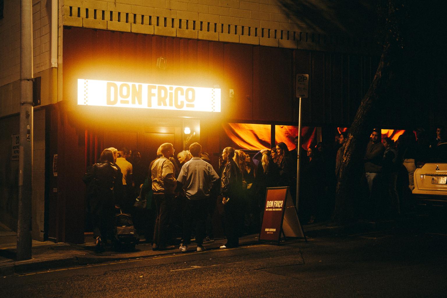 A group of people gathered outside Don Frico restaurant at night, with its illuminated sign visible above the entrance.