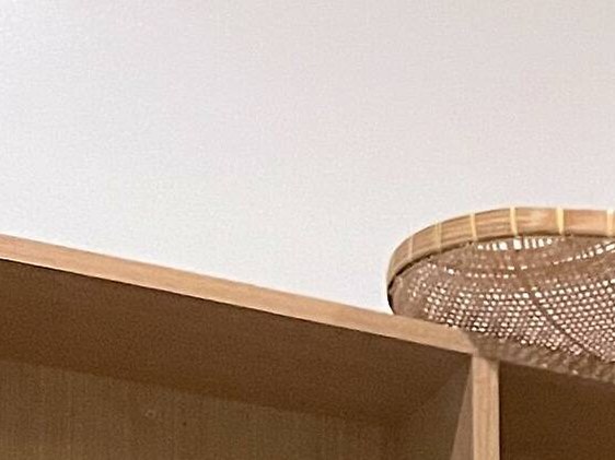 Close-up architectural detail showing the top edge of a wooden shelving unit or counter and a woven rattan/bamboo pendant lamp shade, with no person,