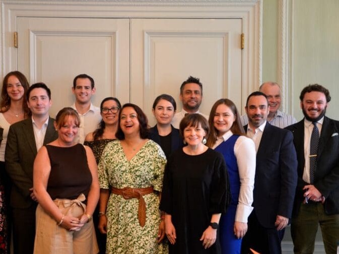 A group of approximately 14-15 professionals, including men and women, in formal attire, smiling and posed for a group portrait.