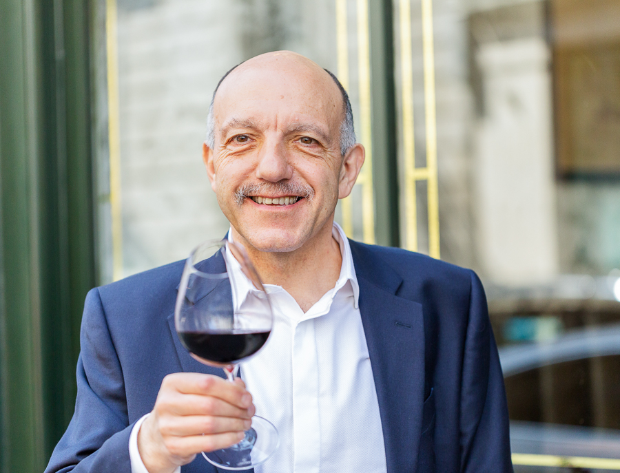 Gérard Basset, a celebrated figure in the wine world, smiles while holding a glass of red wine.