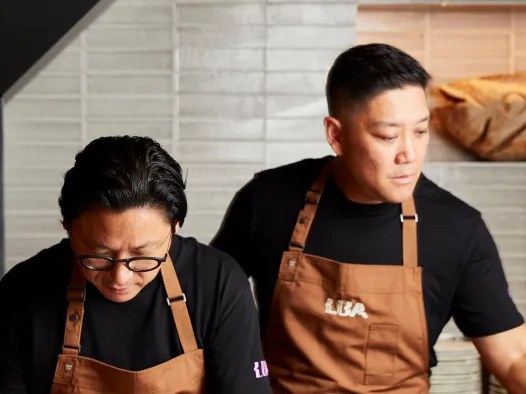 Two chefs in brown aprons working in a kitchen setting.