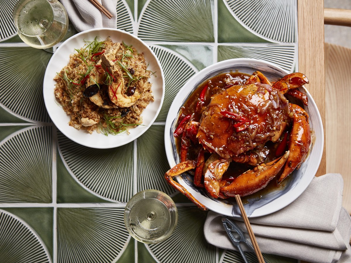 Overhead view of two dishes: a whole crab in chili sauce and fried rice with shrimp, accompanied by white wine and chopsticks.