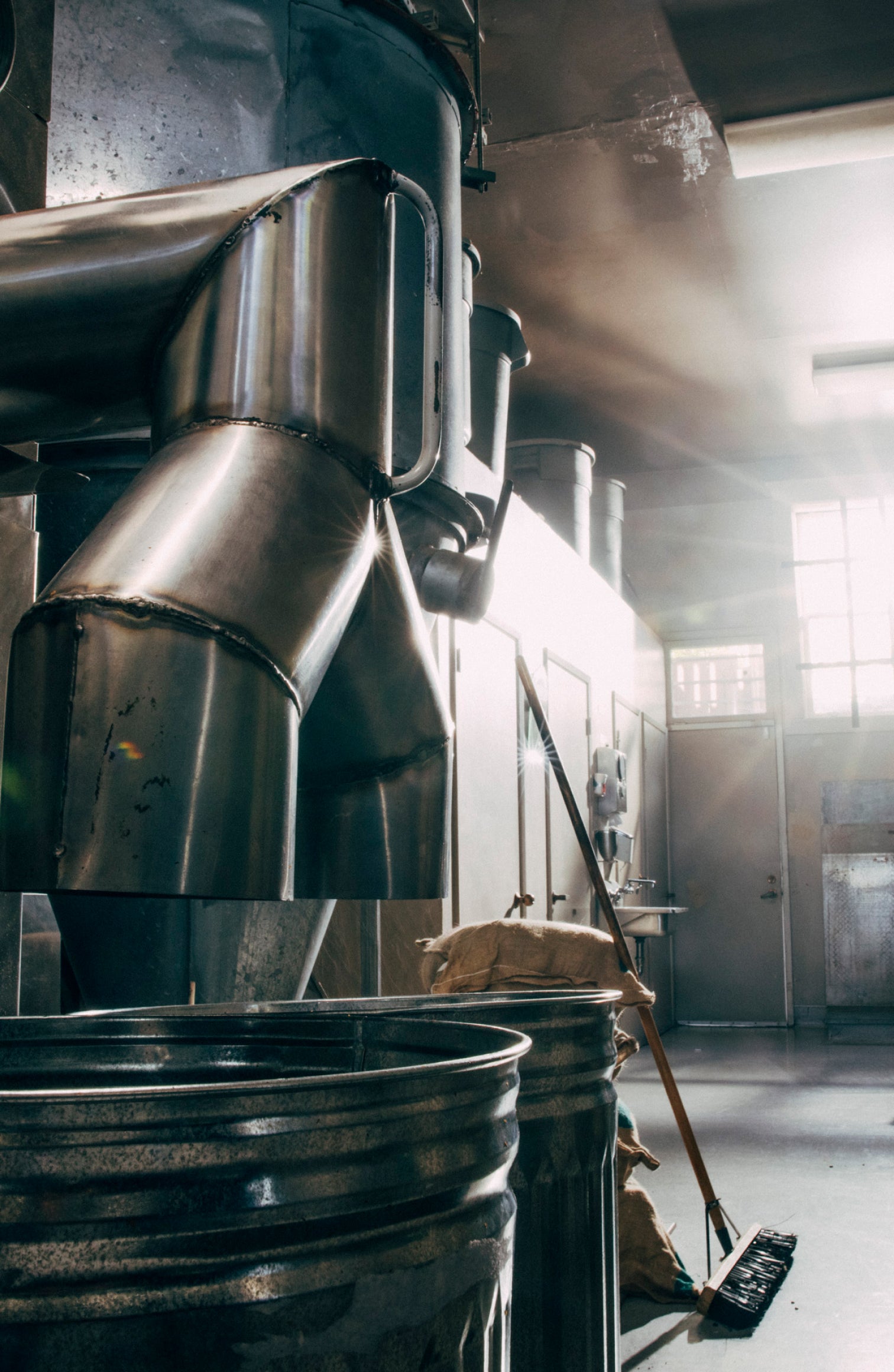 Industrial coffee roasting equipment with stainless steel fluid-bed roaster system in operation, showing steam/vapor rising from the roasting chamber;