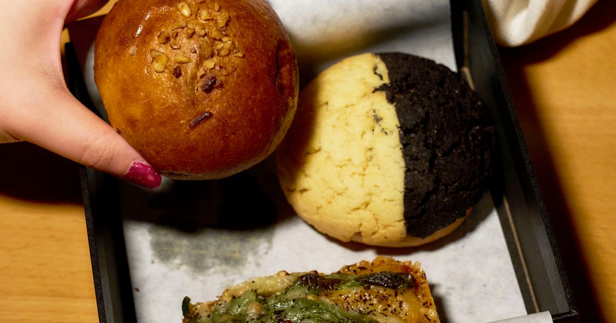 Three artisan bread rolls on a black tray with a hand holding one roll topped with nuts