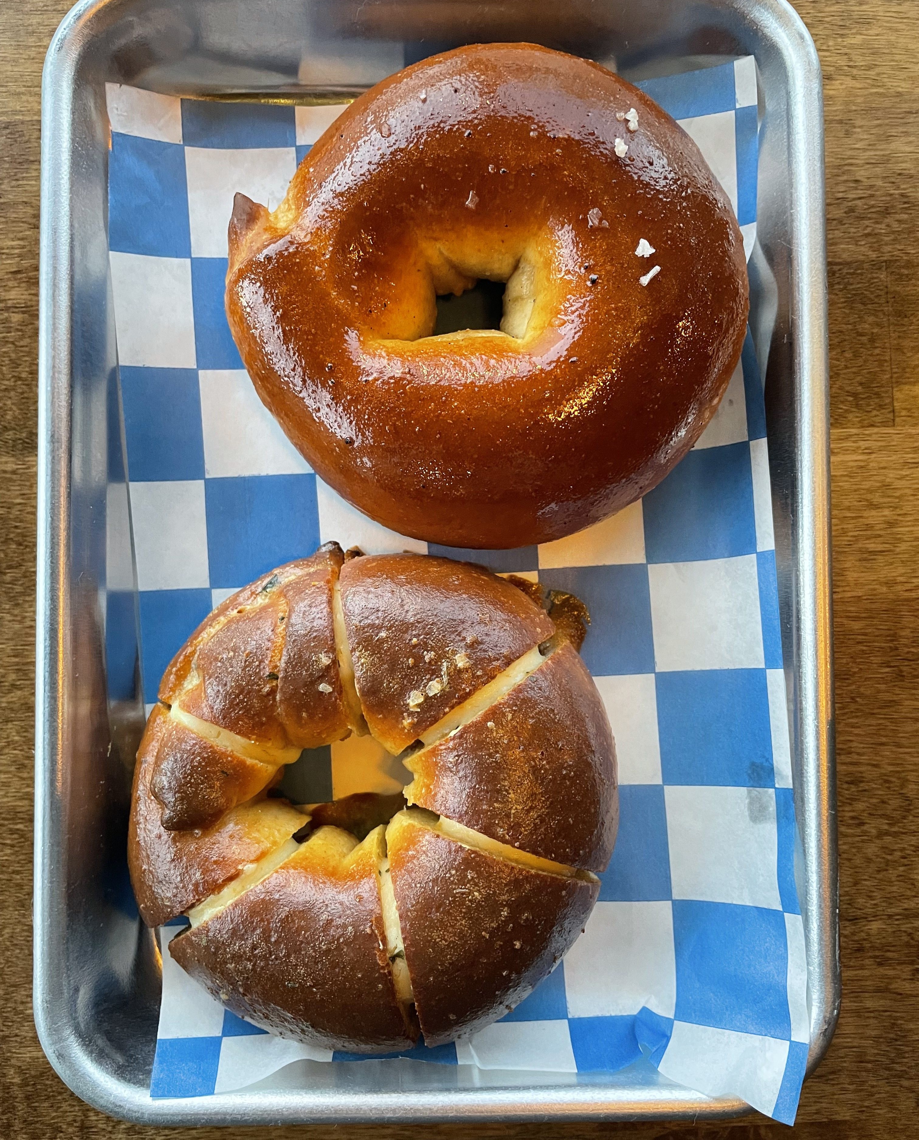 Two golden-brown salt bread rolls on a metal tray with blue checkered paper