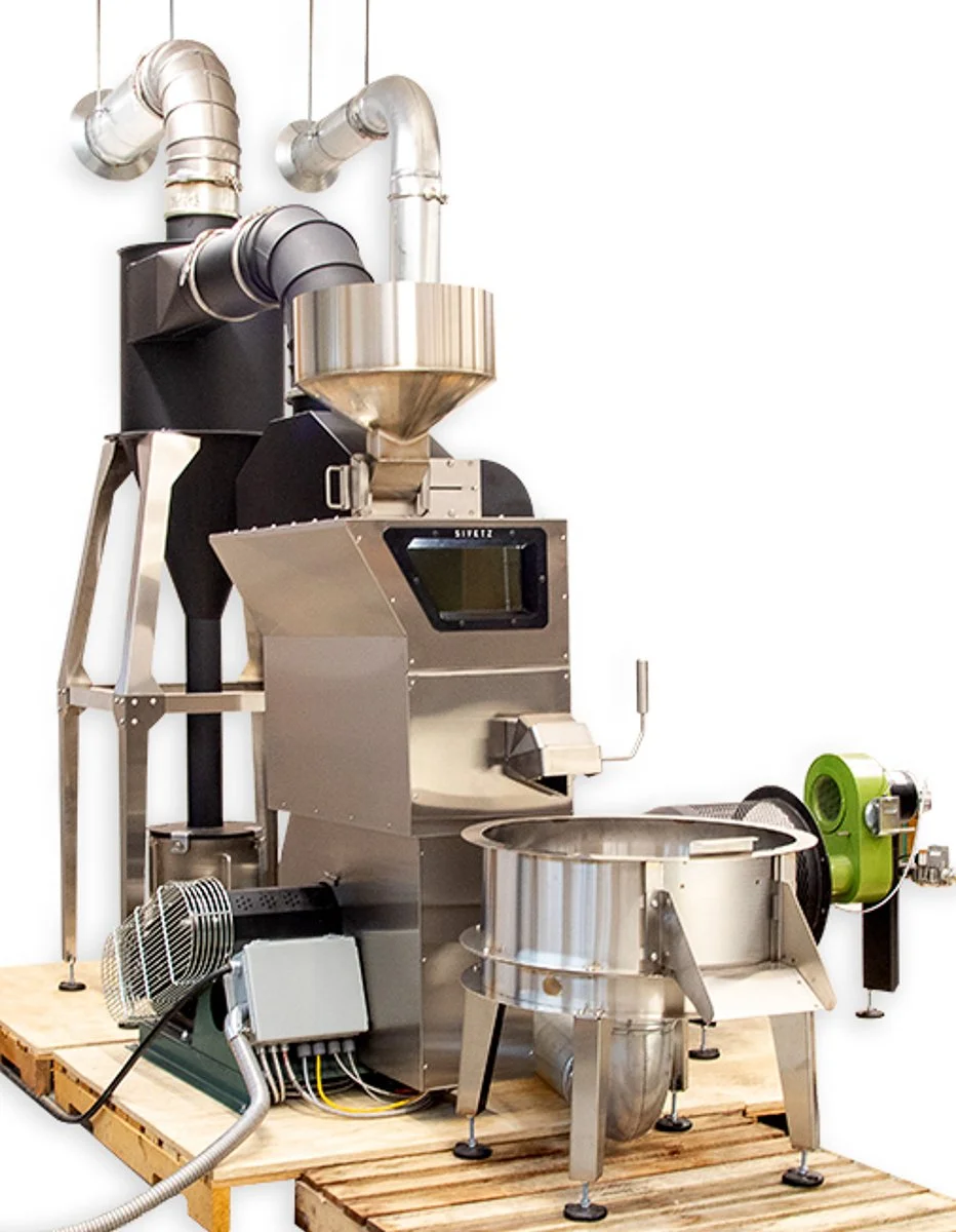 A Sivetz SRM-15 fluid-bed coffee roaster with visible hopper, control panel, and exhaust ducting, mounted on a wooden platform with auxiliary equipmen