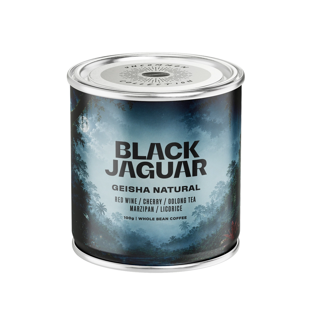 A cylindrical coffee tin labeled 'BLACK JAGUAR GEISHA NATURAL' with flavor notes 'RED WINE / CHERRY / OOLONG TEA / MARZIPAN / LICORICE' and '100g WHOL