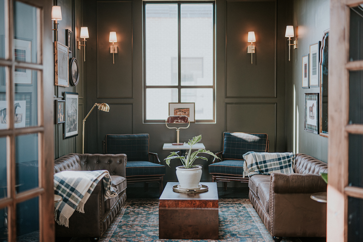 An upscale coffee shop lounge interior with dark green paneled walls, leather seating, wall sconces, and a large window