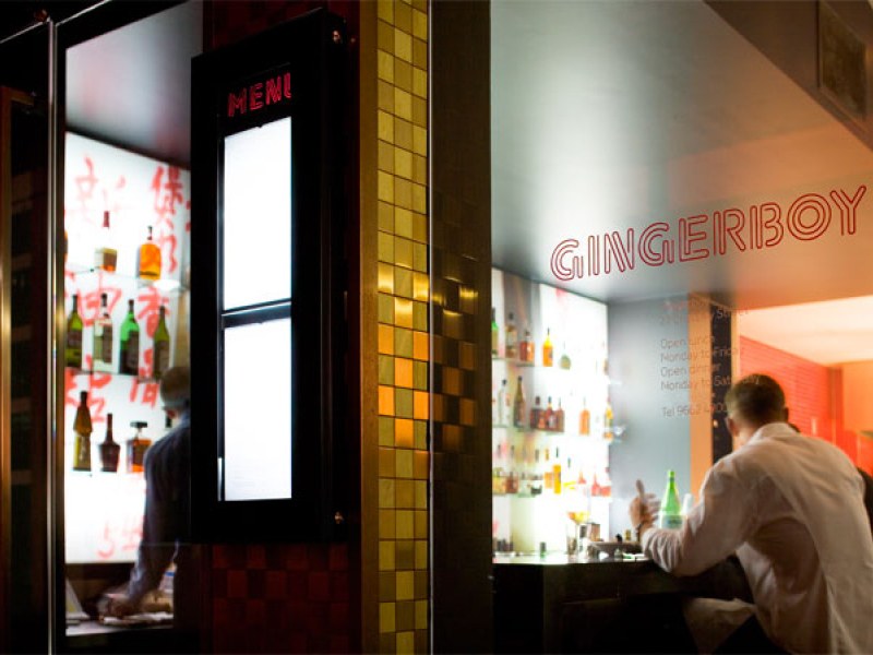 The interior of Gingerboy on Crossley Street, Melbourne, with a gold-tiled facade, illuminated 'MENU' board, and a bartender.