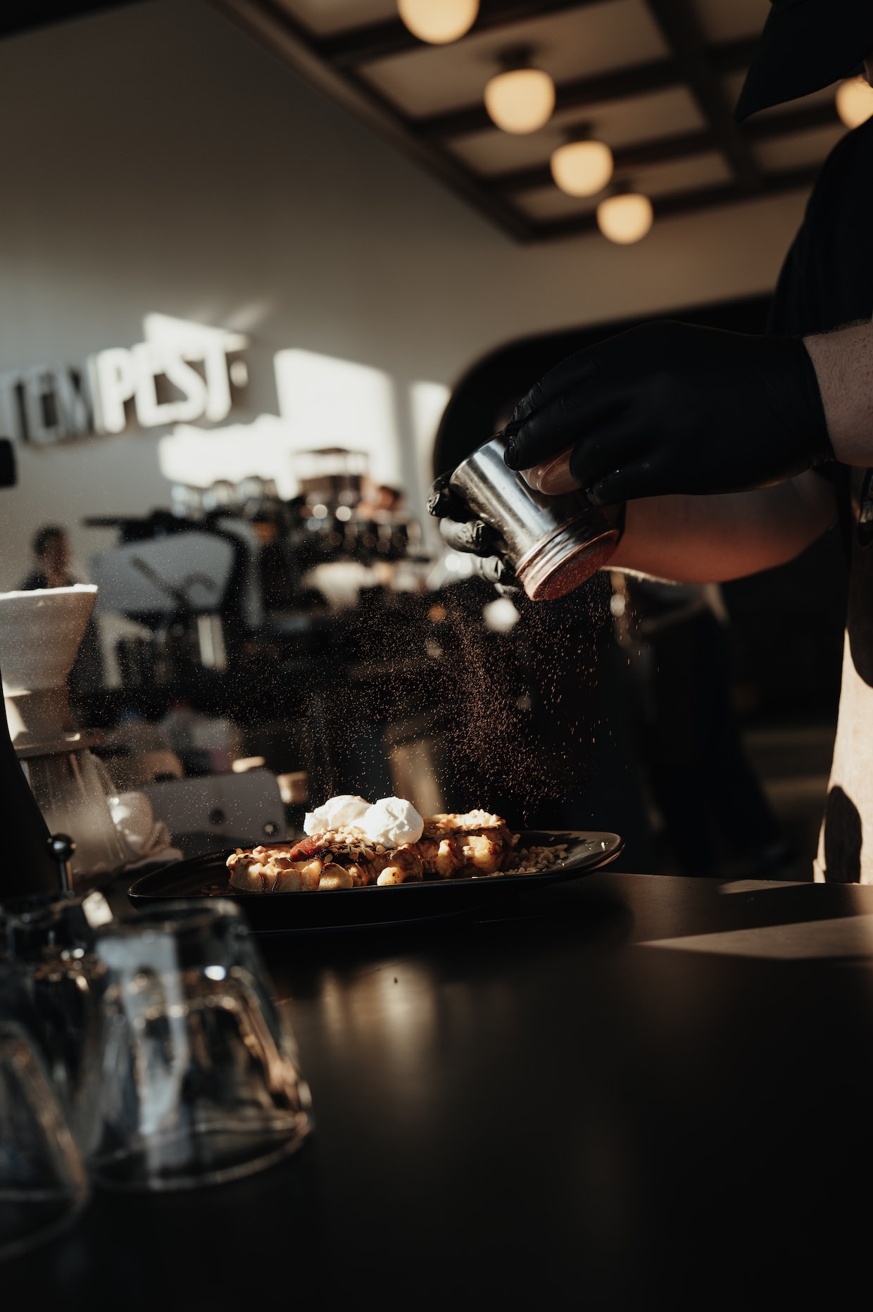 A barista preparing a waffle dish at an espresso bar, with visible coffee equipment and cafe interior