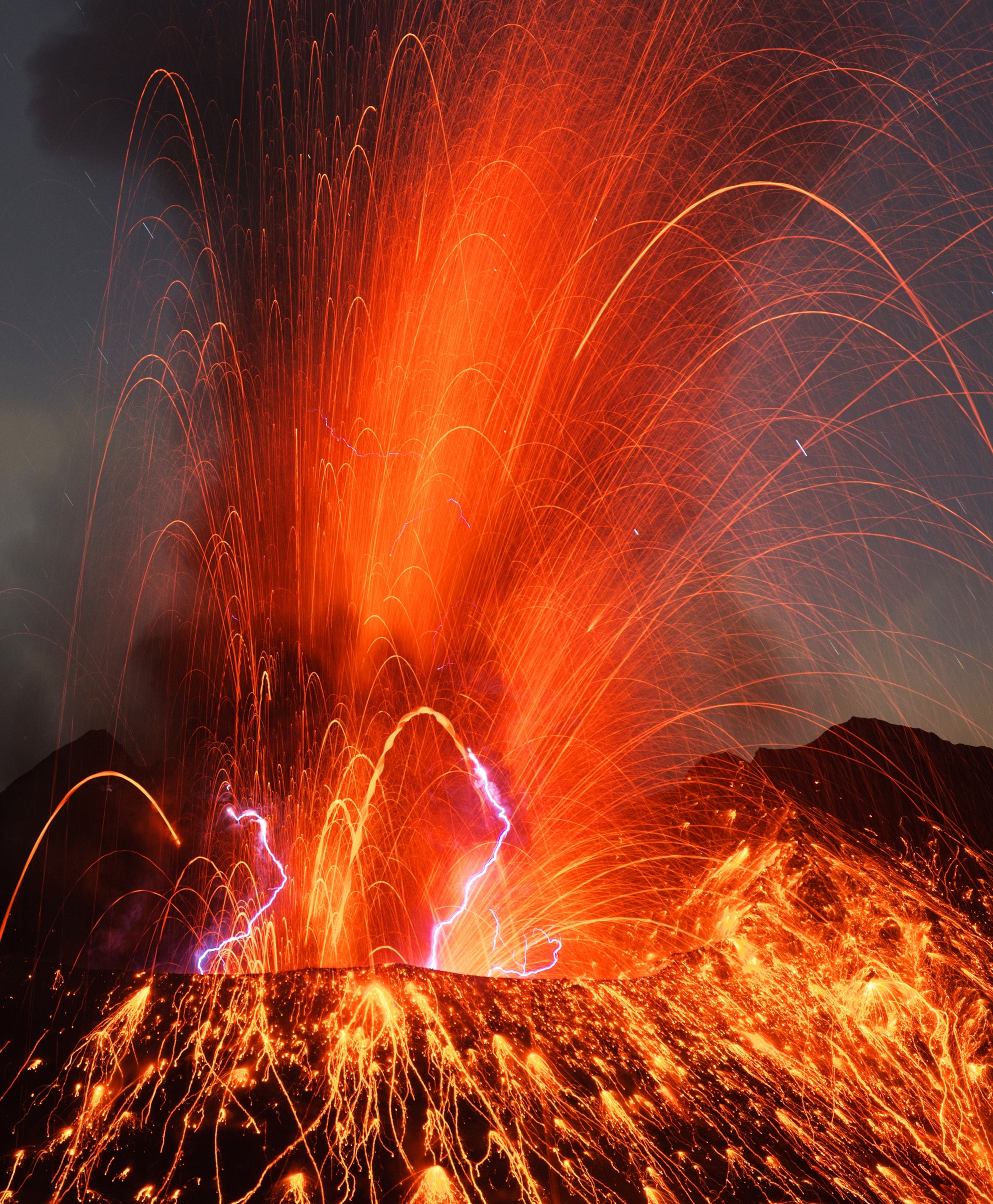 A dramatic nighttime volcanic eruption showing fountains of molten lava and lightning arcing from Sakurajima volcano's crater; National Geographic edi