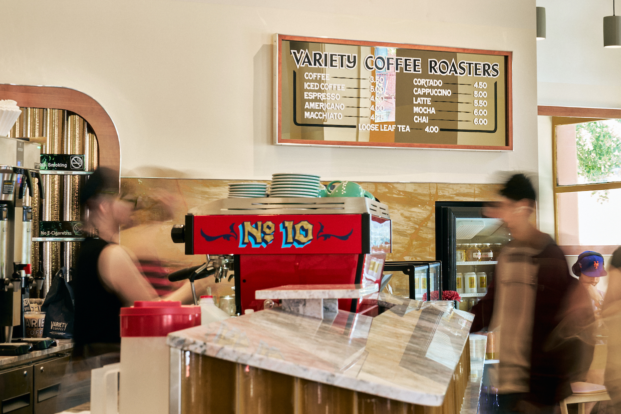 Interior of a coffee shop showing a red La Marzocco espresso machine with visible signage reading 'VARIETY COFFEE ROASTERS' on the menu board, matchin
