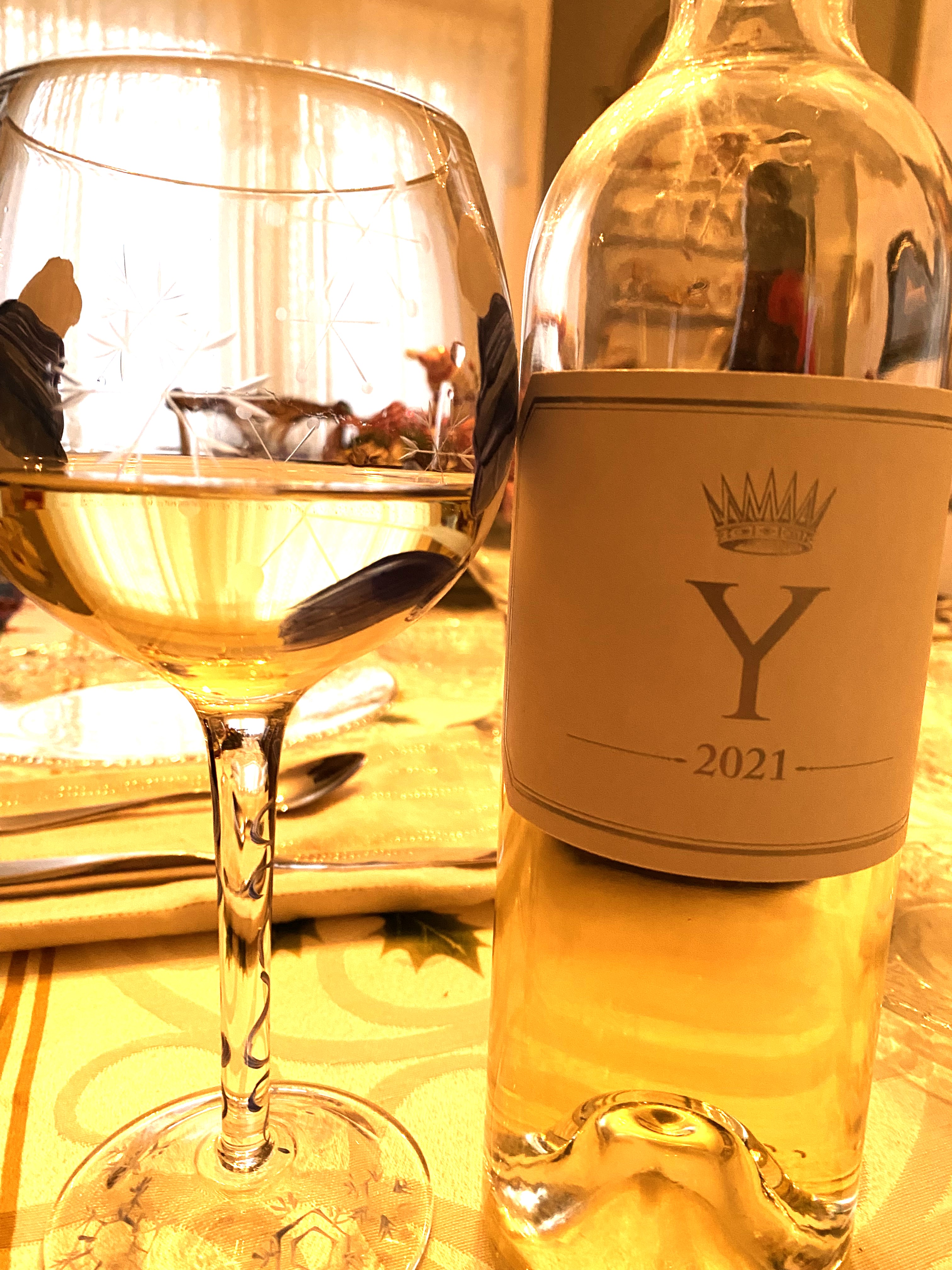 Y 2021 wine bottle and poured glass with golden liquid on table setting with place settings