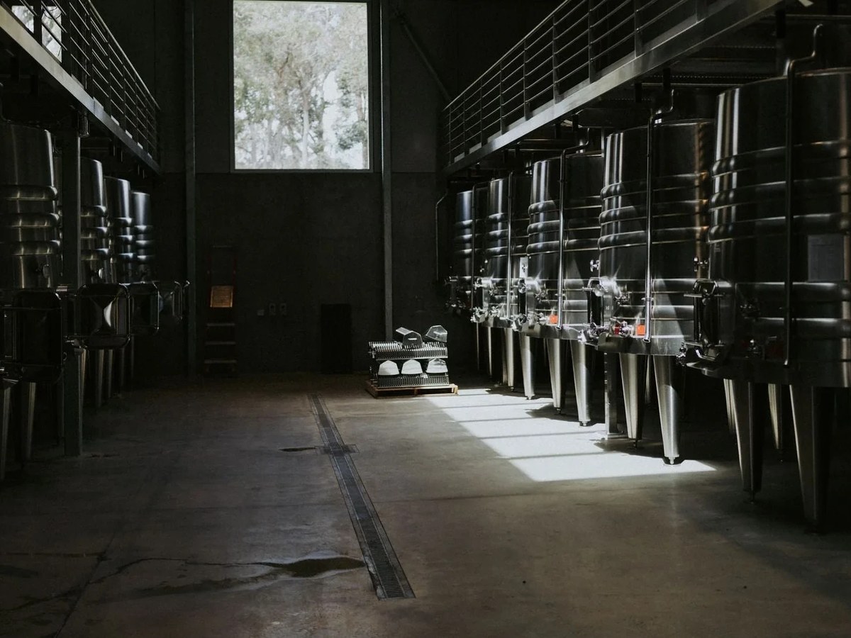 A modern winery interior with rows of tall, gleaming stainless steel fermentation tanks on both sides of a central aisle.