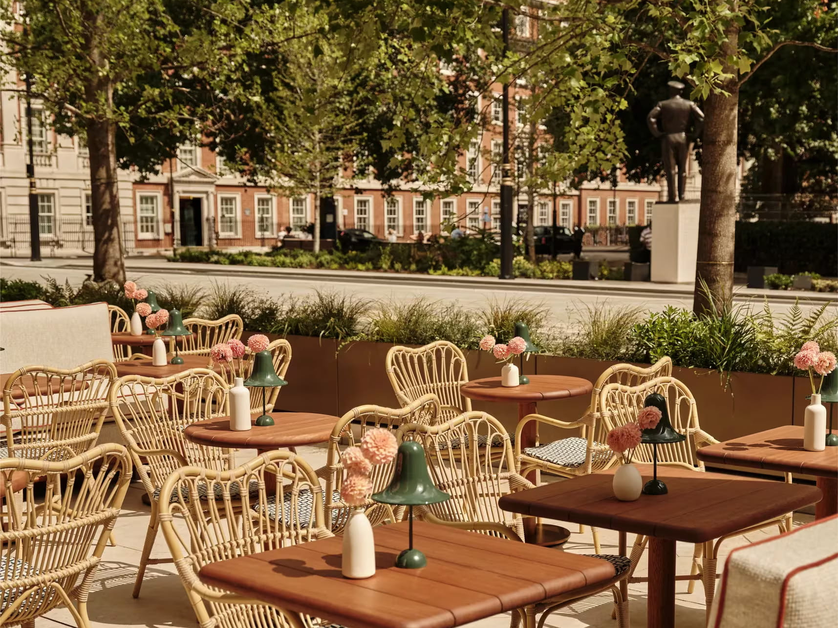 Outdoor cafe patio of GSQ restaurant at The Chancery Rosewood with wicker chairs, wooden tables, and pink flowers in vases. Greenery and trees surround the setting. Calm and inviting atmosphere.