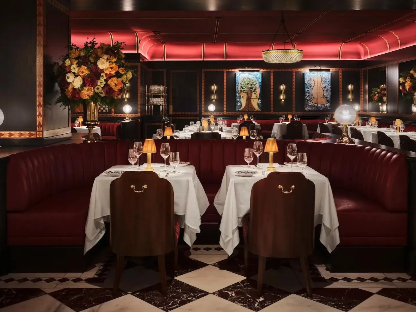 Elegant interior of Carbone London at The Chancery Rosewood with red leather booths and white tablecloths. Warm lighting, floral arrangements, and colorful artwork create a cozy ambiance.