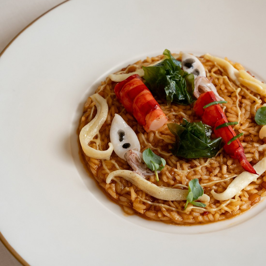 A gourmet seafood risotto on a white plate, topped with shrimp, squid, and greens. The dish is elegantly arranged with vibrant colors.