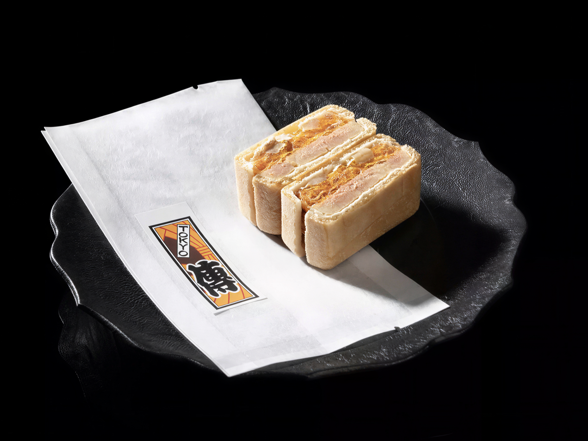 Wafers with cream filling on a black plate with white paper, labeled "TOKYO" in bold letters. The setup is elegant, minimalist.