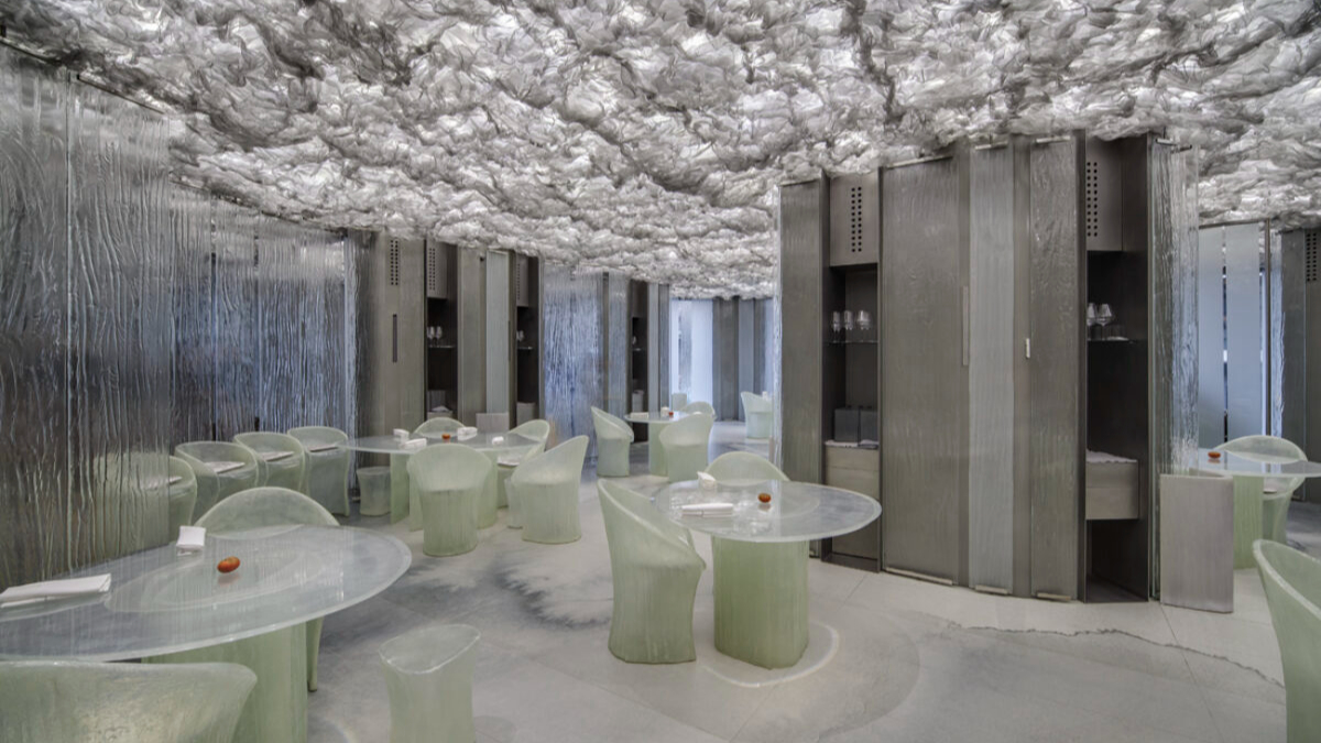 Futuristic restaurant with translucent tables, chairs, and cloud-like ceiling. Cool tones dominate the serene, modern ambiance. No people present.