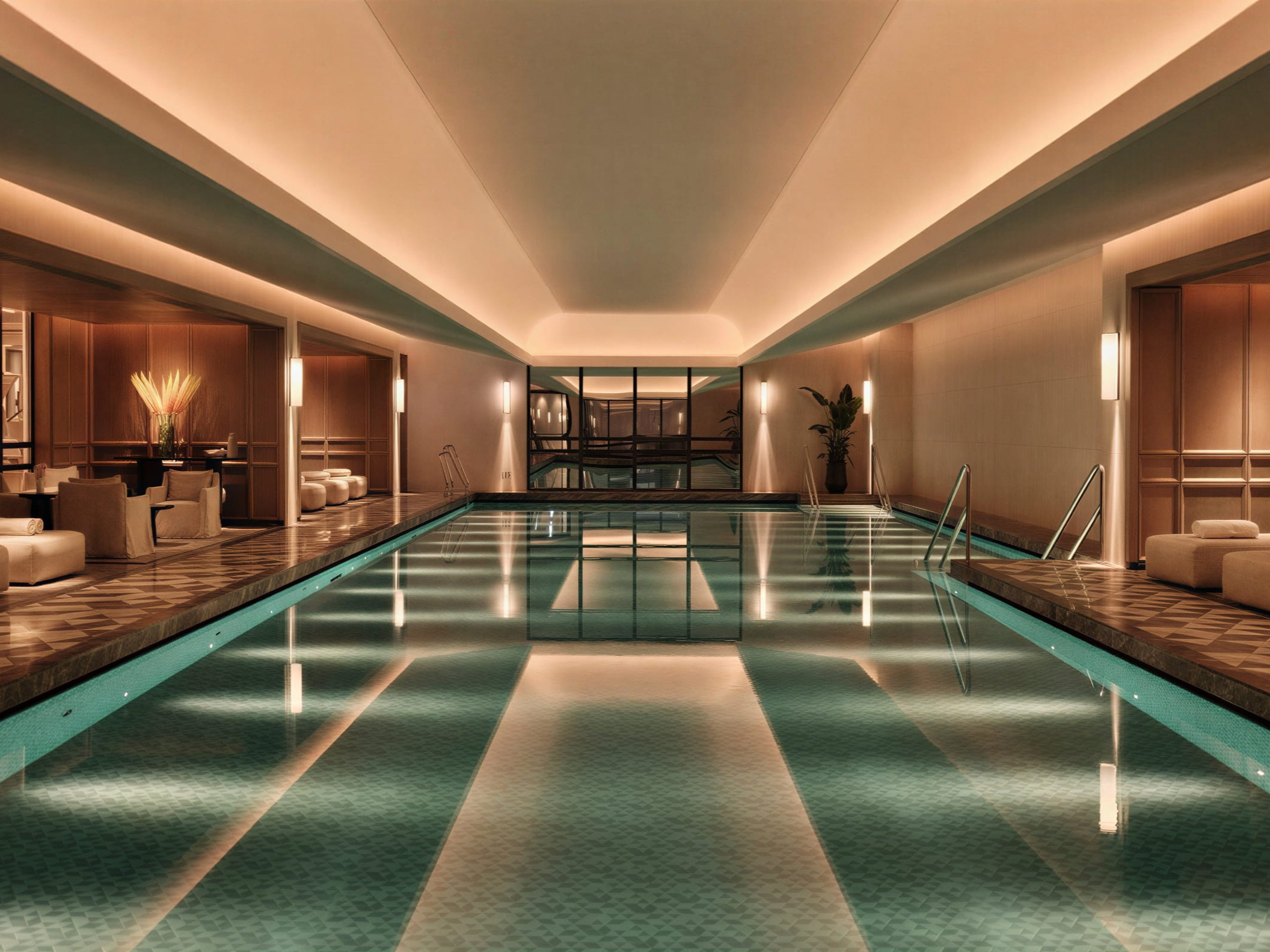 Luxurious indoor pool at the spa at The Chancery Rosewood with serene lighting. Elegant seating areas and plants line the sides, with reflections on the calm water surface.