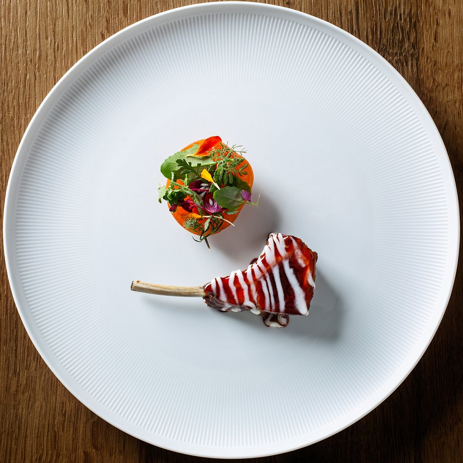 Elegant dish with a colorful salad and glazed meat on a large white plate. Wooden table surface adds warmth to the minimalist presentation.