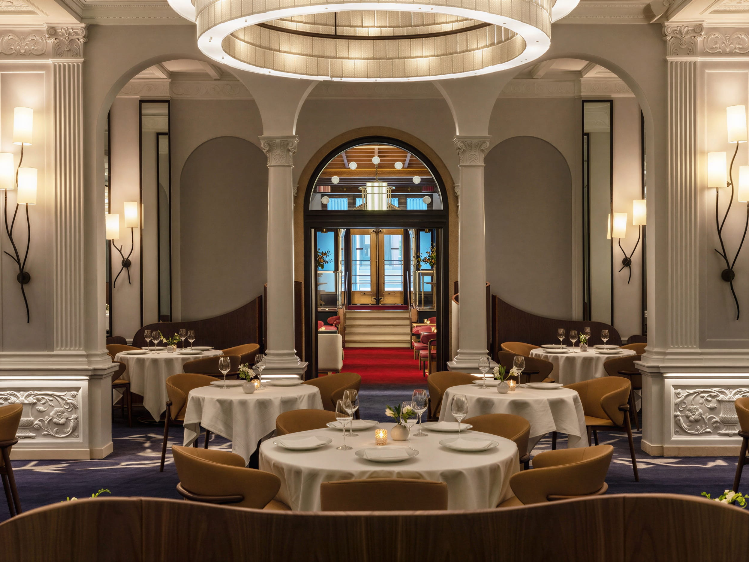 Elegant interior dining room at Daniel NYC with round tables set for dining, beige chairs, white tablecloths, ornate columns, and soft wall lighting.