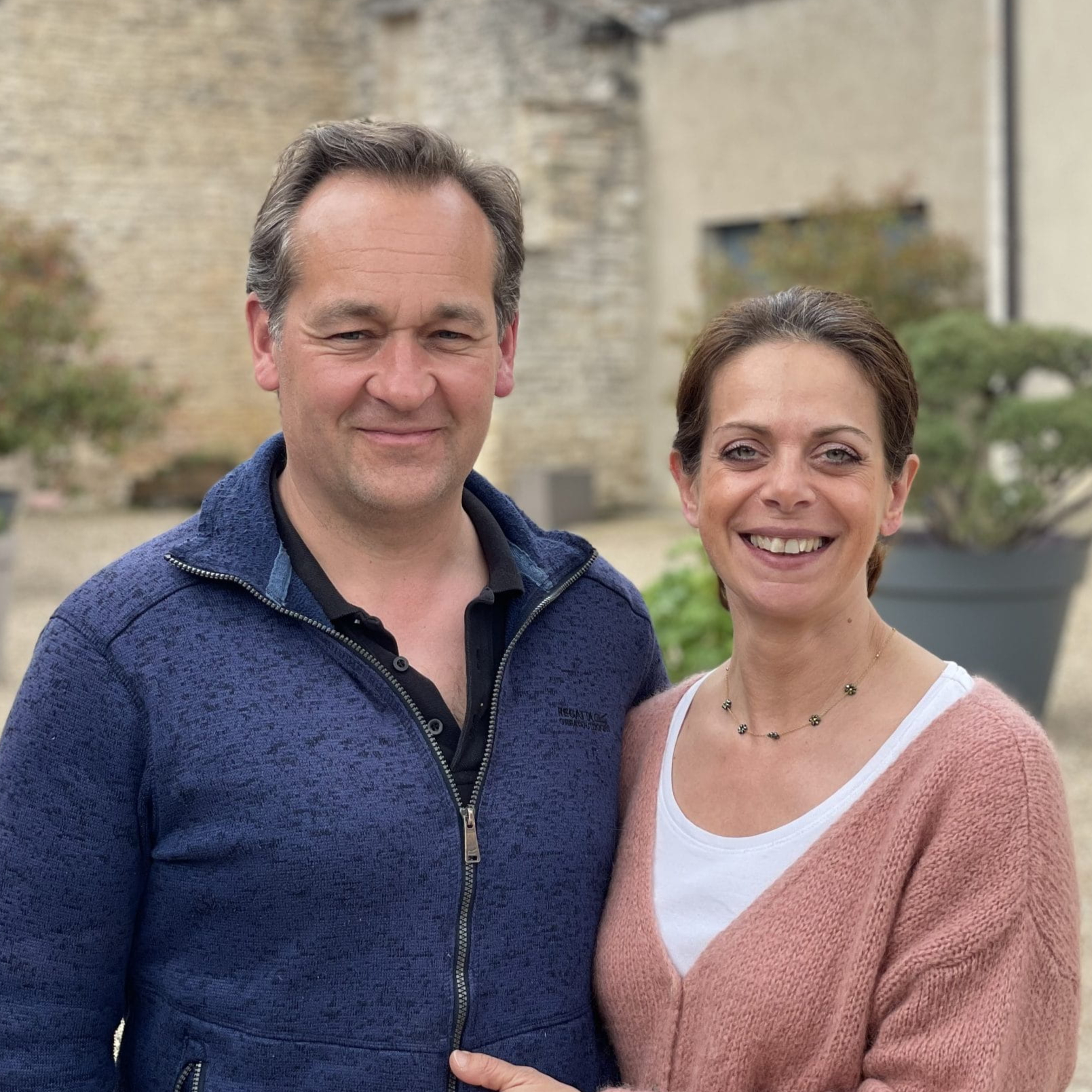 Winemaker Alex Moreau and his wife wear nice clothes and stand outside a historic stone french chateau