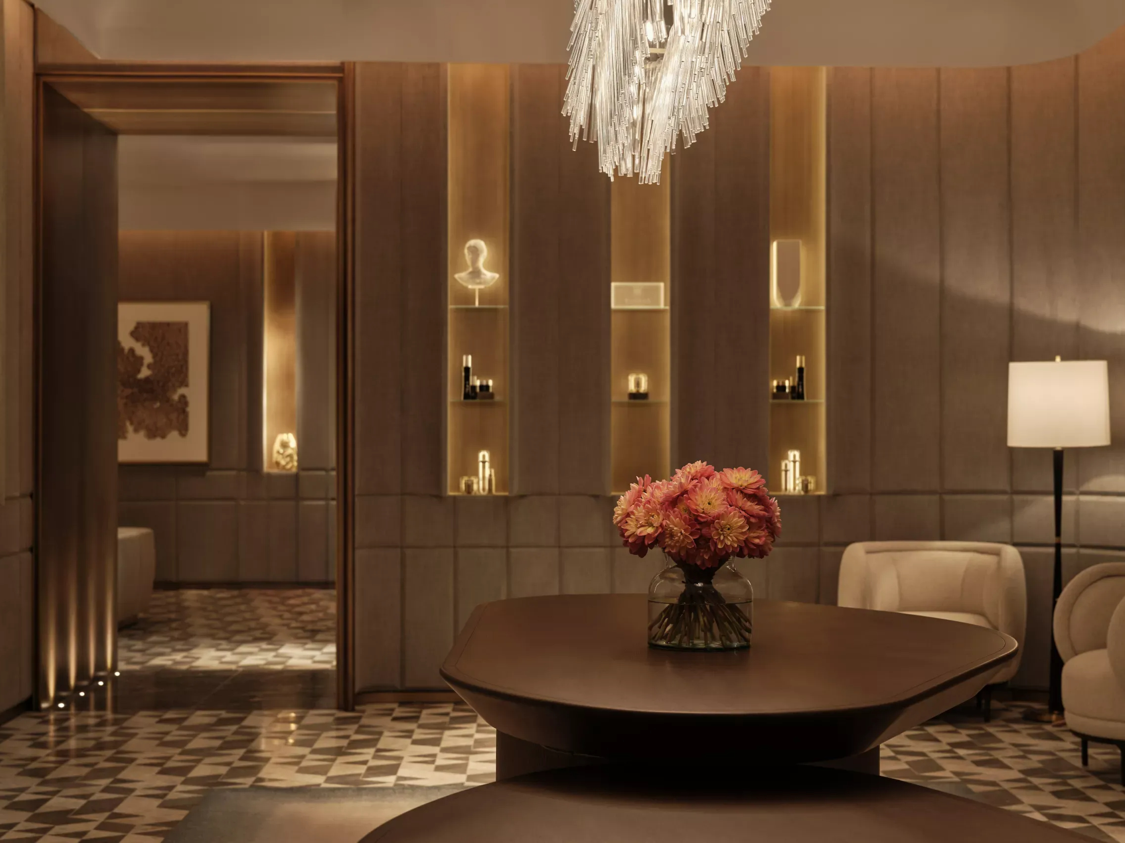 Elegant Asaya Spa Lobby at The Chancery Rosewood with a chandelier, wood paneling, art on wall. A large table with pink flowers is in the center. Soft lighting creates a cozy mood.