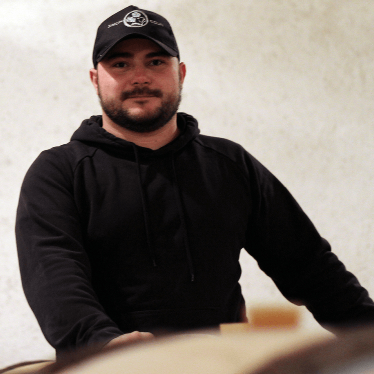 Winemaker Simon Colin stands in his barrel room wearing a black cap and a black hoody.