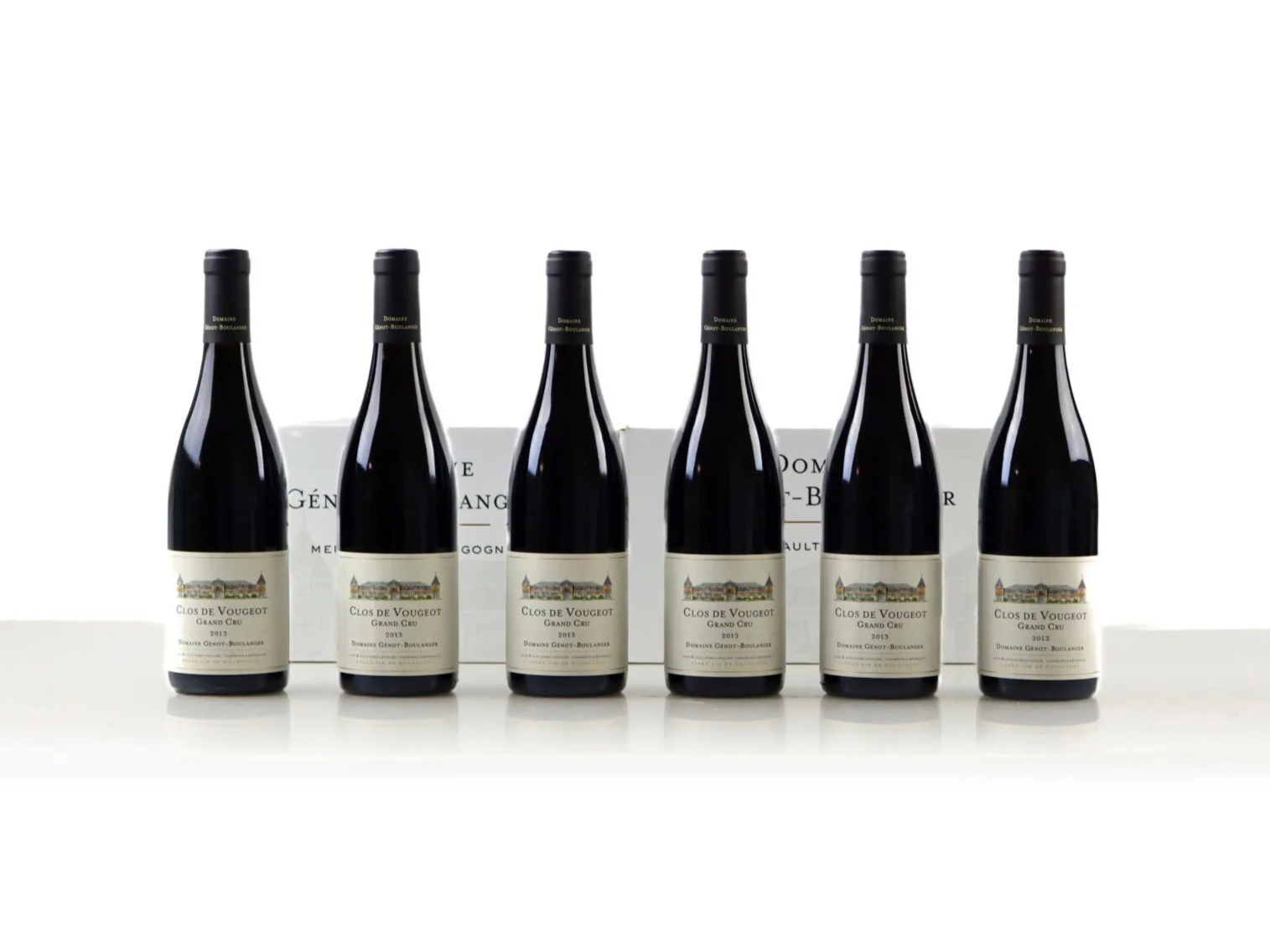 Six wine bottles of 2013 Domaine Génot-Boulanger Clos de Vougeot Grand Cru are lined up on a white surface. Two boxes are visible in the background.