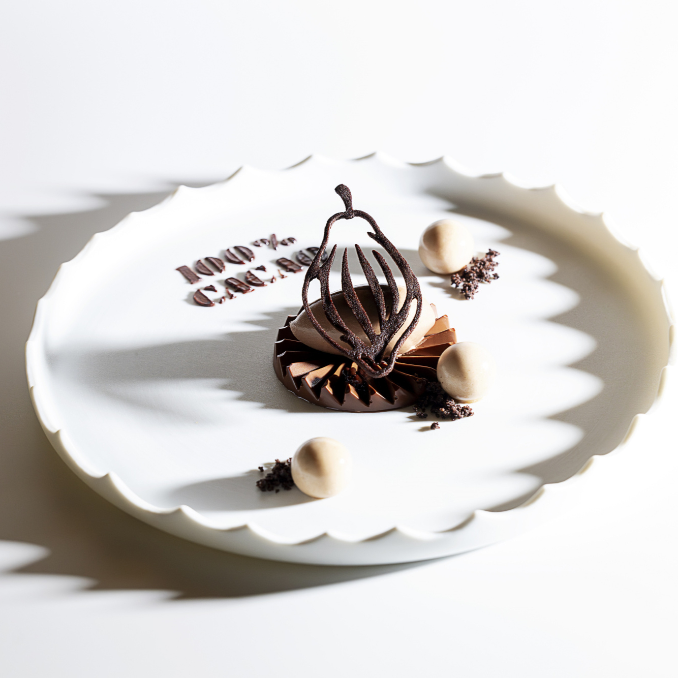Elegant dessert on white plate, featuring chocolate artistry and "100% Cacao" text. Shadows create a delicate pattern, evoking sophistication.