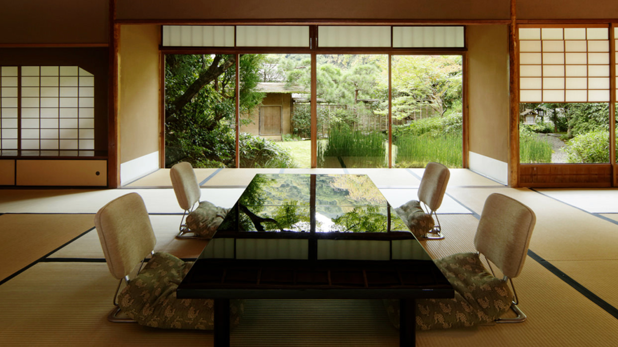 Japanese tea room with tatami mats, a black table, and cushioned seating. Sliding doors open to a lush garden view, creating a serene mood.